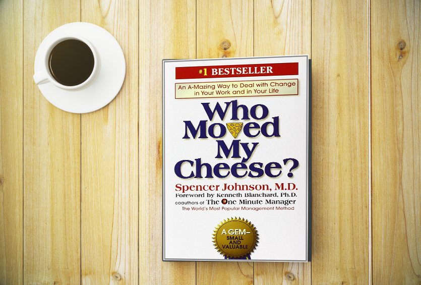 Book cover of who moved my cheese sitting on a table with a cup of coffee.
